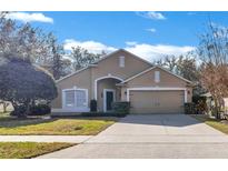 Tan one-story house with two-car garage and lush landscaping at 900 Khingan Ct, Apopka, FL 32712