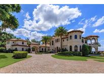 Stunning exterior view of a Mediterranean-style home with a brick driveway, lush landscaping, and palm trees at 11900 Lake Butler Blvd, Windermere, FL 34786