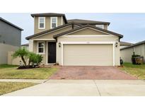 Two-story house with tan siding, a two-car garage, and a brick driveway at 494 Amadoras Way, St Cloud, FL 34771