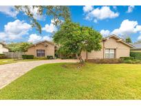 Tan house with a paved driveway, landscaping, and a large tree in the front yard at 615 Tuskawilla Point Ln, Winter Springs, FL 32708