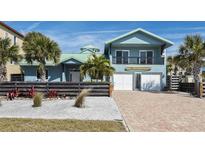 Two-story beach house with a teal exterior, a brick driveway, and a landscaped front yard at 6111 Turtlemound Rd, New Smyrna Beach, FL 32169