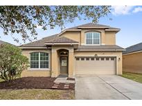 Two-story house with tan exterior, two-car garage, and landscaping at 7525 Azalea Cove Cir, Orlando, FL 32807