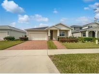 Tan house with a brick driveway and walkway, two-car garage, and landscaping at 2514 Park Ridge St, Apopka, FL 32712