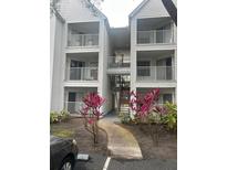 Three-story condo building with balconies and landscaping featuring vibrant red plants leading to a sidewalk at 11568 Westwood Blvd # 1034, Orlando, FL 32821