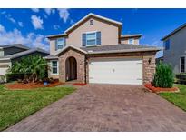 Two-story home with a stone facade, blue shutters, and a two-car garage on a brick paved driveway at 17013 Tradewind Pt, Winter Garden, FL 34787