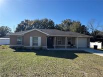 One-story house with a brown exterior, a garage, and a well-maintained lawn at 14476 Se 34Th Ct, Summerfield, FL 34491