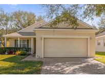Beige home featuring a two-car garage and a brick paver driveway, with manicured landscaping and inviting curb appeal at 2513 Castle Pines St, Clermont, FL 34711