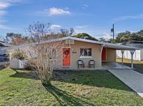 Tan mid-century modern home with orange door, landscaped lawn, and long driveway at 1514 Doreen Ave, Ocoee, FL 34761