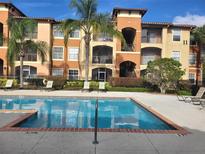 Community pool and building featuring lounge chairs and tropical landscaping on a sunny day at 5518 Metrowest Blvd # 104, Orlando, FL 32811