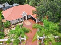 Stunning aerial view of home with barrel tile roof, paver driveway, lush landscaping, and serene lake views at 120 W Magnolia Ave, Howey In The Hills, FL 34737