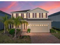 Two-story home featuring tan siding, red shutters, a brick driveway and an attached two-car garage at 613 Bloom Ter, Davenport, FL 33837