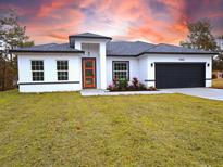 Modern home featuring a gray roof, orange front door, dark garage door, and nicely manicured landscaping at 17825 Sw 34Th Ter, Ocala, FL 34473