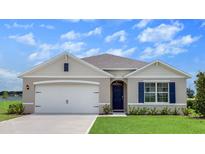 Charming single-story home featuring a two-car garage, blue shutters, manicured lawn, and a welcoming front entrance at 2117 Pigeon Plum Dr, Haines City, FL 33844