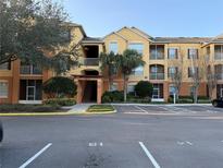 Attractive condo building with yellow and brown facade, landscaping, and ample parking at 8775 Sartori St # 303, Orlando, FL 32829