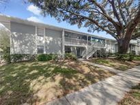 Two-story condo with painted gray exterior, a large tree, and a communal staircase to the screened in porches at 700 E Airport Blvd # C7, Sanford, FL 32773