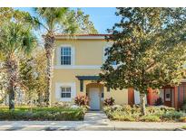 Charming yellow two-story townhouse featuring a well-maintained front yard with lush greenery and palm trees at 8452 Crystal Cove Loop, Kissimmee, FL 34747