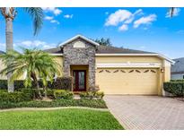 Charming single-story home features a two-car garage, stone accents and lush landscaping under a sunny sky at 9848 Nonacrest Dr, Orlando, FL 32832