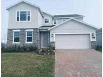 Two-story home featuring stone accents, a brick driveway, a two-car garage, and manicured landscaping at 5961 Vision Rd, St Cloud, FL 34771