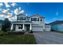Charming two-story home with manicured lawn, gray siding, three-car garage, and brick paver driveway at 674 Creeping Fig St, Apopka, FL 32703