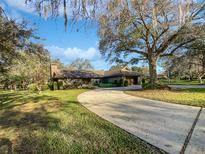 Inviting single-story brick home with circular driveway and mature trees on a well-manicured lawn at 112 Woden Way, Winter Haven, FL 33884