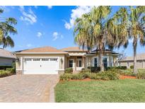 Charming single-story home showcasing a well-manicured lawn, palm trees, and a brick driveway leading to a two-car garage at 10144 Lake Miona Way, Oxford, FL 34484