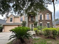 Two-story brick home featuring a stone facade and shuttered windows, surrounded by lush landscaping at 10446 Stone Glen Dr, Orlando, FL 32825