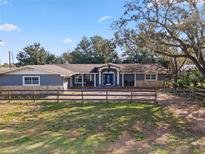 Charming home with a light blue facade, stone accents, a wooden fence, and mature shade trees at 37224 Apiary Rd, Grand Island, FL 32735