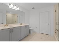 Bright bathroom featuring a double vanity with gray cabinets and quartz countertop, with tile flooring and glass-enclosed shower at 1629 Hill Park Dr, Deltona, FL 32725