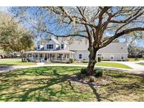 Charming light grey home featuring a large wrap-around porch and mature shade trees at 5150 Banana Point Dr, Okahumpka, FL 34762