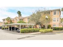 Exterior view of a peach-colored building with covered parking and manicured landscaping at 13500 Turtle Marsh Loop # 839, Orlando, FL 32837