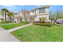 Charming two-story townhome featuring a lush green lawn, manicured bushes, and a cozy entrance with an archway at 9017 Dogleg Dr, Davenport, FL 33896