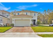 Two-story home featuring a two-car garage, brick driveway, well-manicured lawn, and neutral-colored exterior at 5237 Royal Point Ave, Kissimmee, FL 34746