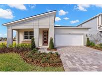 Modern home with a red front door, white trim, a brick driveway, a 2-car garage, and manicured landscaping at 9292 Sea Pine Ave, Orlando, FL 32832