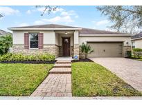 Charming home featuring a stone facade, tan siding, and a well-manicured lawn with a brick walkway and driveway at 8807 Tatara St, Orlando, FL 32836