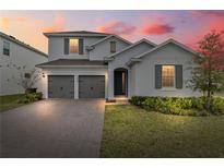 Charming two-story home with gray shutters, a brick driveway, and manicured landscaping at dusk at 4484 Lions Gate Ave, Clermont, FL 34711