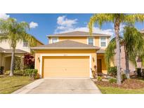 Two-story home with a two-car garage, lush landscaping, and vibrant yellow facade at 2613 Santosh Cv, Kissimmee, FL 34746