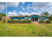 Charming single-story home featuring a red front door, well-maintained lawn, and blue and beige exterior paint at 36010 Kalamazoo Dr, Eustis, FL 32736