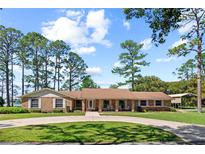Charming brick home with a circular driveway, manicured lawn, mature trees and rocking chairs on the covered front porch at 5203 Pineview Way, Apopka, FL 32703