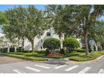 View of The Cloisters community entrance featuring a sign, lush landscaping, trees, and the building's exterior at 100 S Interlachen Ave # 304, Winter Park, FL 32789
