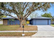 Charming single-story home featuring a bright yellow front door, stone accents, mature tree, and a two-car garage at 1005 Leeds Ct, Winter Park, FL 32792