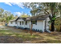 Charming exterior view of a freshly painted white brick home with gray accents and mature trees in the front yard at 1343 Spring Lake Rd, Fruitland Park, FL 34731