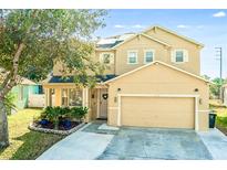 Charming two-story home with manicured landscaping, tan paint, and solar panels on the roof at 1602 Pine Ridge Dr, Davenport, FL 33896