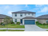 Two-story home with a blue garage door, well-manicured lawn, and solar panels on the roof at 630 Citrus Isle Blvd, Davenport, FL 33837