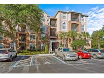 Three-story condo building with multiple balconies, lush trees, and parking, all under a bright blue sky at 1357 Venezia Ct # 402, Davenport, FL 33896