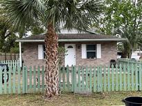 Charming brick home featuring a manicured lawn, a quaint picket fence, and a mature palm tree at 2600 Elm Ave, Sanford, FL 32773