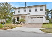 Two-story home featuring a manicured lawn, brick driveway, and attached two-car garage at 14384 Alafaya Oak Bnd, Orlando, FL 32828