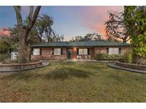 Charming brick home featuring a lush front lawn, mature trees, and quaint outdoor seating at 4227 Spring Ln, Lakeland, FL 33811