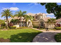 Beautiful two-story home with a well-manicured lawn and lush landscaping, including palm trees and a brick driveway at 11234 Willow Gardens Dr, Windermere, FL 34786