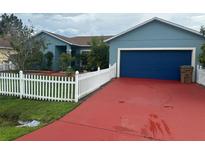 Charming single-story home with blue exterior, red driveway, blue garage door and white picket fence at 214 Great Yarmouth Ct, Kissimmee, FL 34758