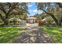 Stately brick home with white columns, gated entrance, and mature trees lining the driveway creating a picturesque view at 2525 Cr 543, Sumterville, FL 33585